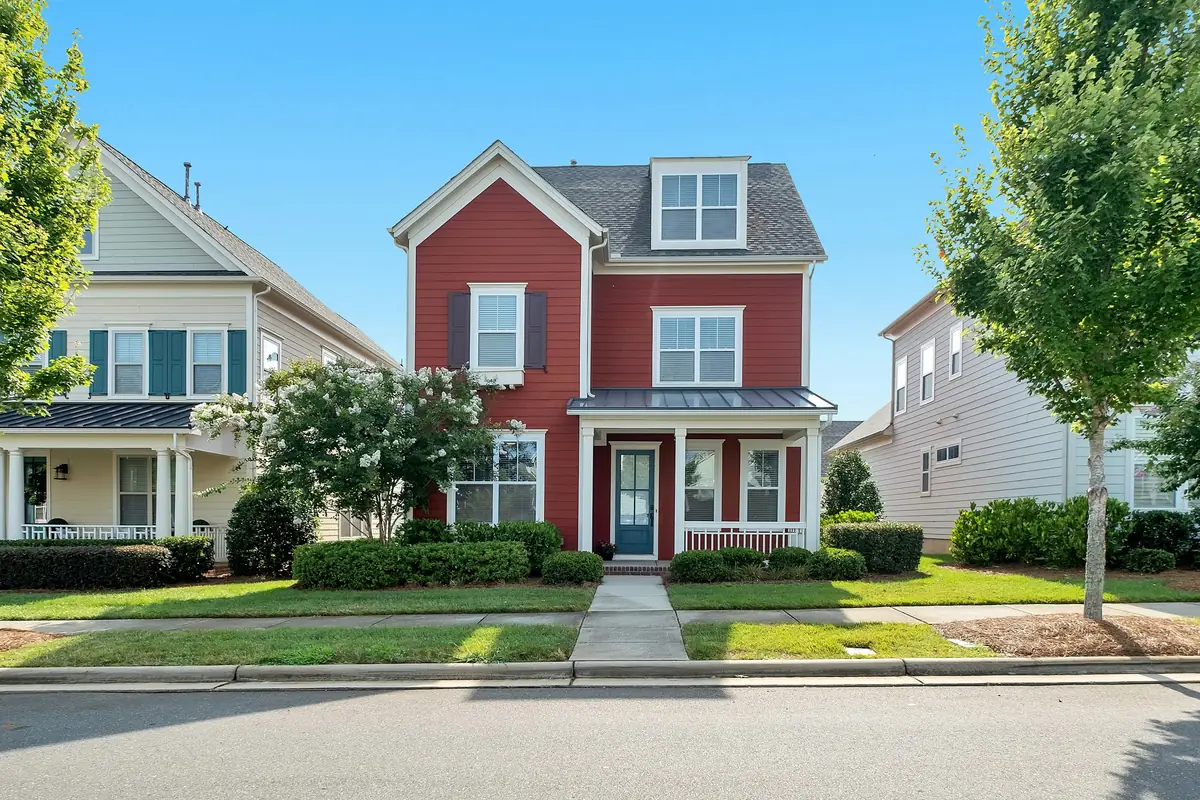 Three-story house with red lap siding, white trim, dark shutters and a teal front door under a blue sky