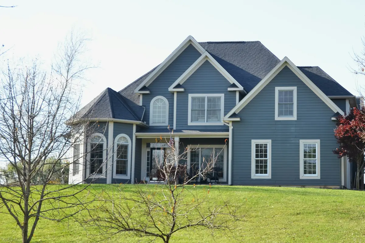 Two-story house with slate-blue siding, white trim and arched windows above a sloping green lawn