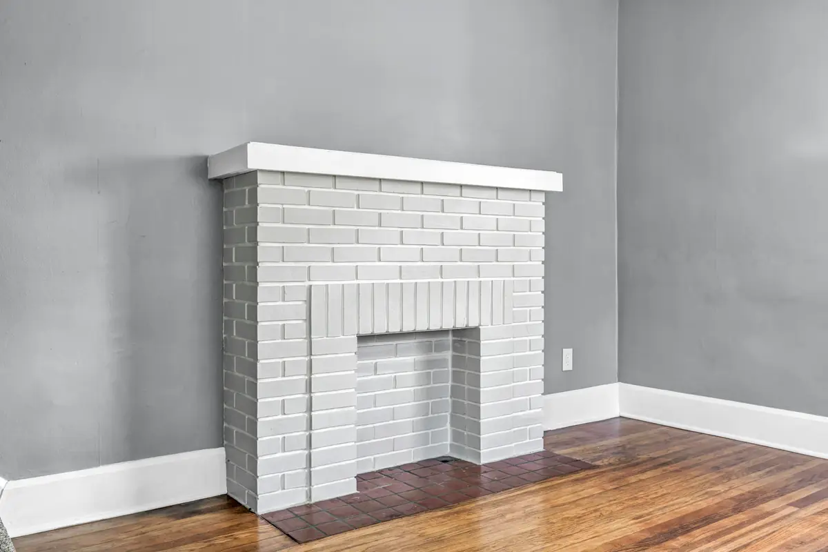 Brick fireplace painted white, with a white mantel shelf and a dark tile hearth, against gray walls on a wood floor