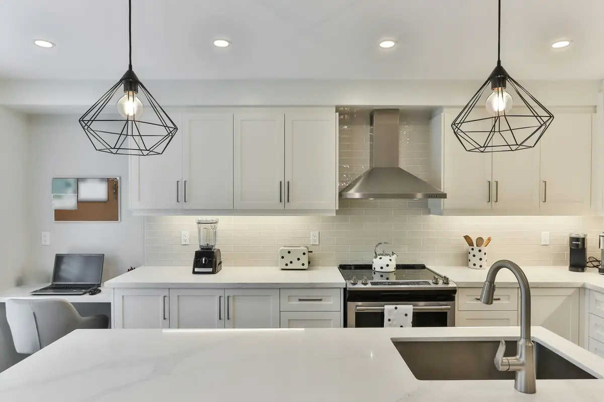White shaker kitchen cabinets with a subway tile backsplash, a stainless range hood and black wire pendant lights