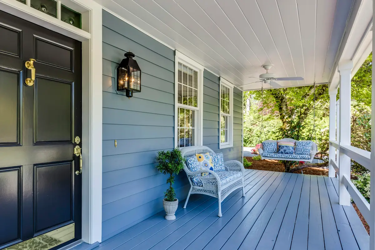 Covered porch with blue-gray lap siding, a white beadboard ceiling, a black front door and white wicker seating