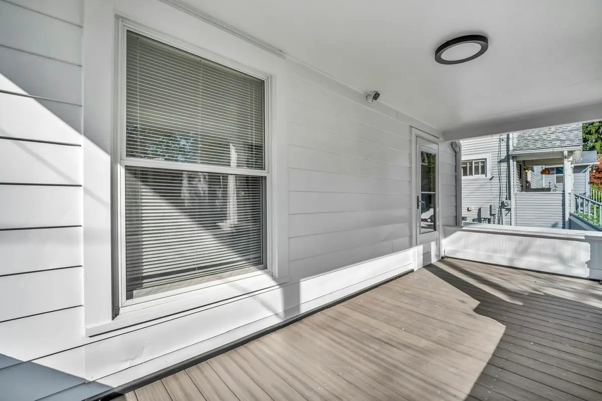 Covered porch with white lap siding, a white ceiling with a round light and a gray plank floor in afternoon sun