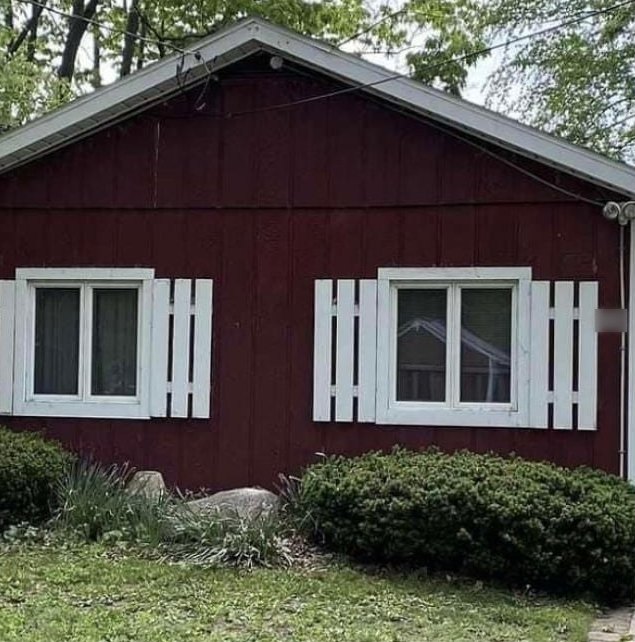 Cottage with faded red board-and-batten siding and white shutters, before painting