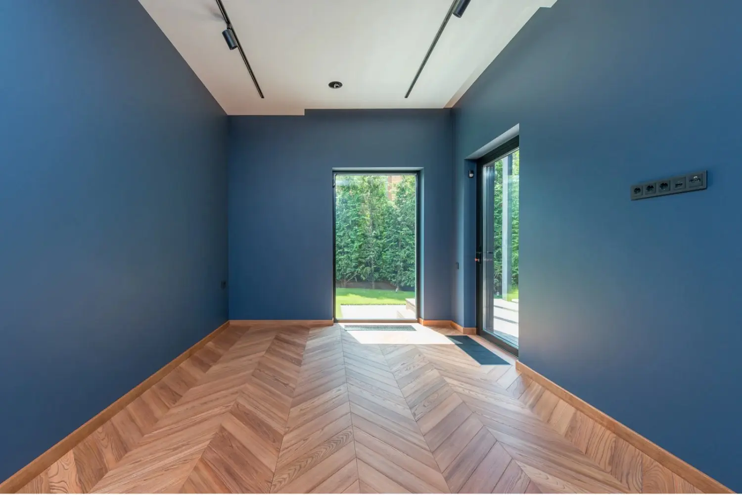 Empty room with deep blue walls, a white ceiling and a chevron wood floor