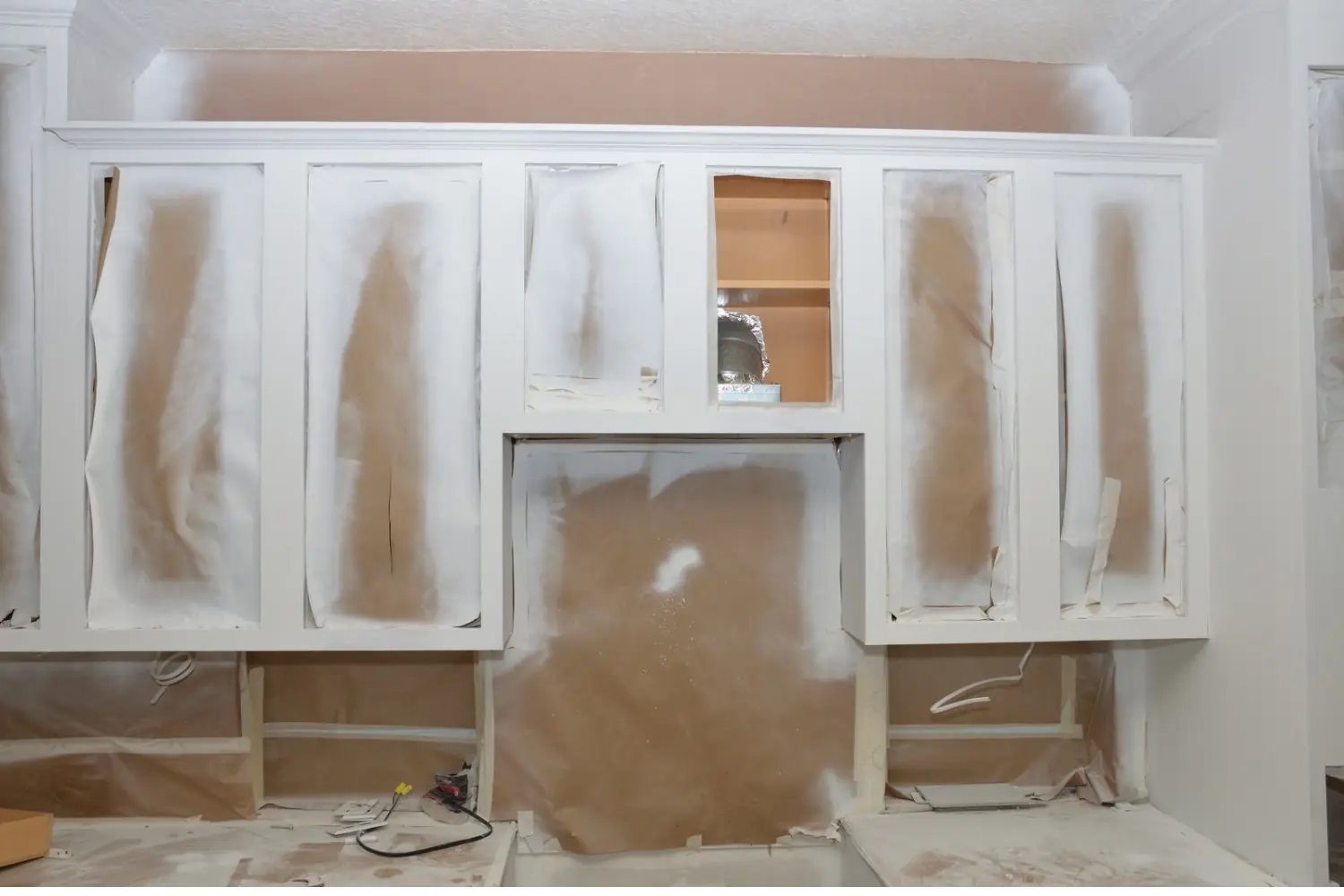 Kitchen cabinet frames sprayed white, with the door openings and the wall behind masked in paper