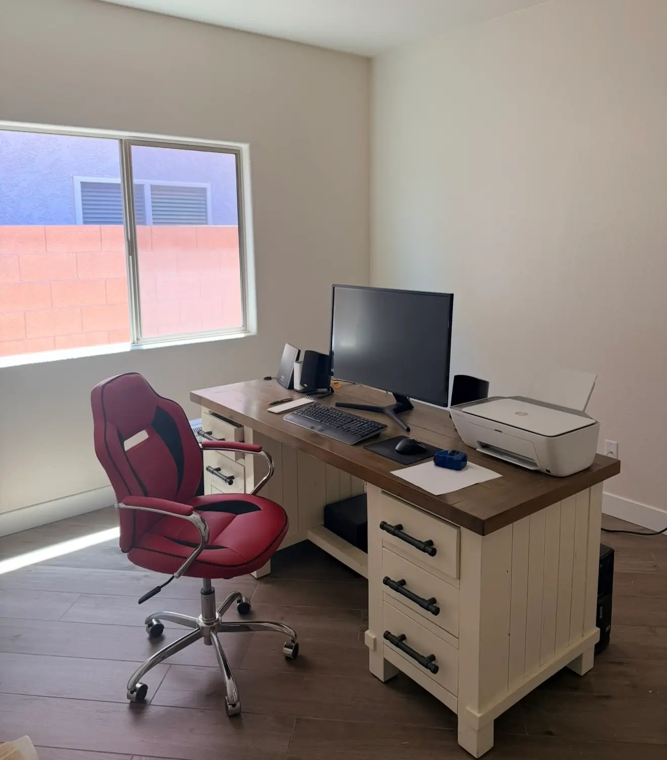 Home office with off-white walls, a farmhouse desk and a red office chair, after painting