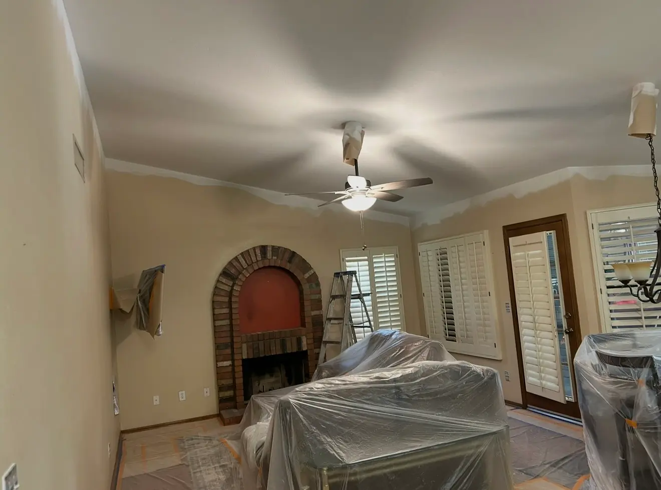 Living room mid-repaint with the ceiling painted, furniture wrapped in plastic and the floor covered