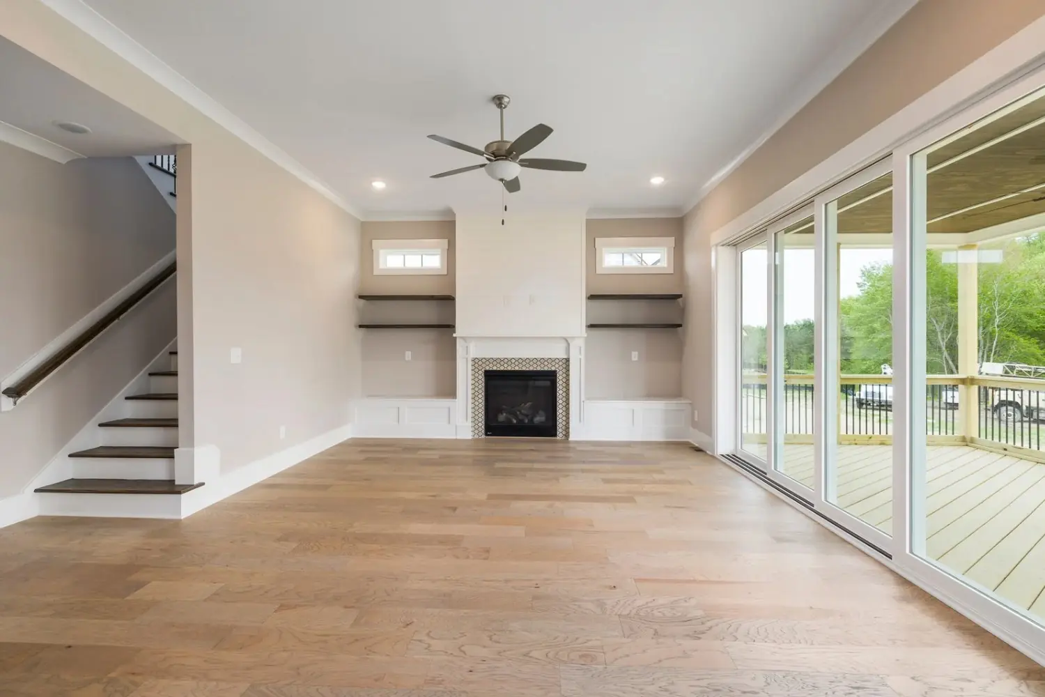 Empty living room with greige walls, white trim, a fireplace between built-in shelves and a staircase