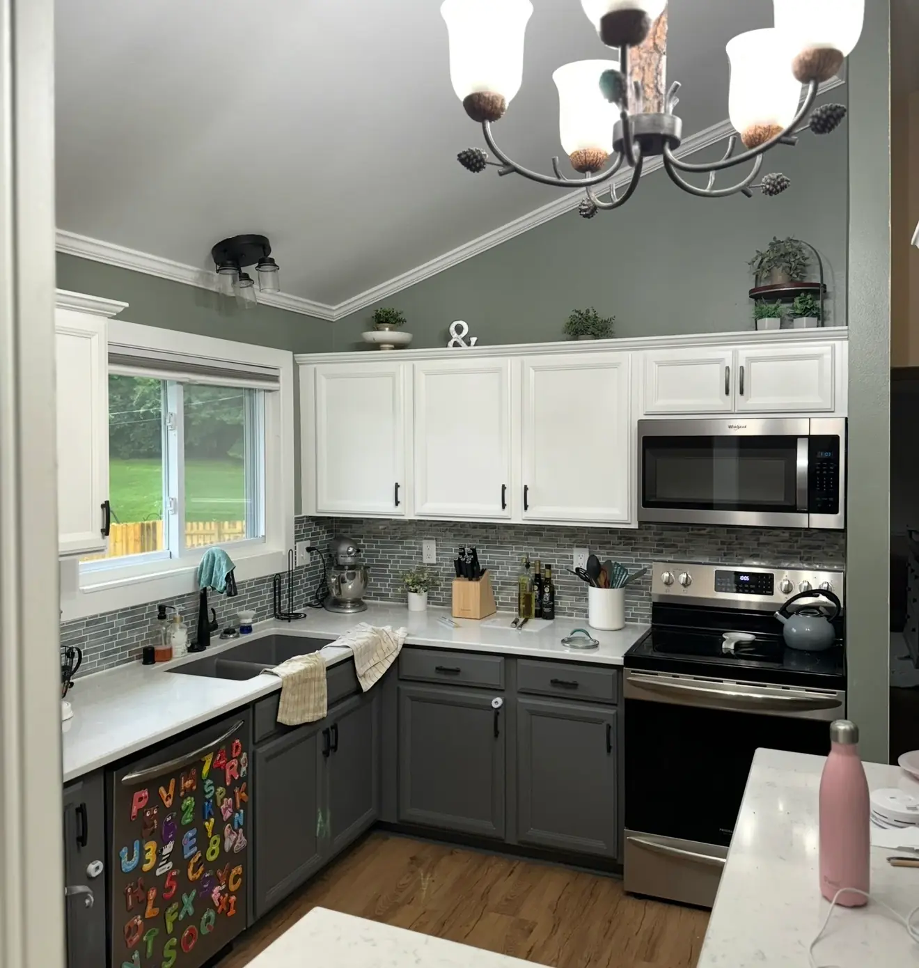 Kitchen with white upper cabinets, gray lower cabinets and sage-green walls under a vaulted ceiling